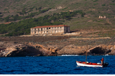 Boat near coastal building and rocky landscape.