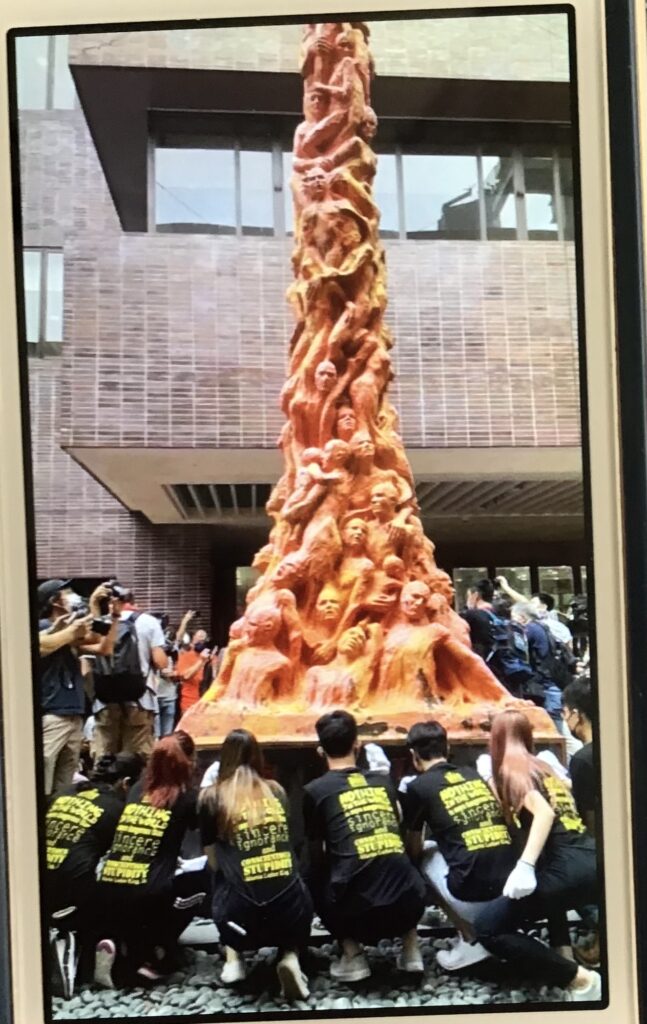 People gathered around tall sculpture with faces.