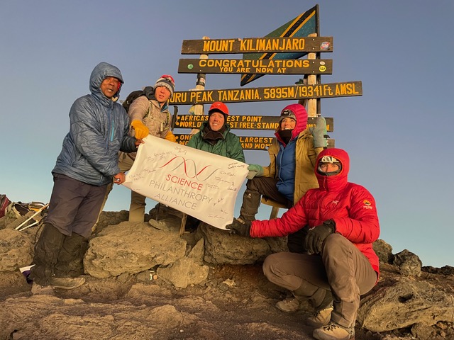 Group of hikers posing at Mount Kilimanjaro summit sign.